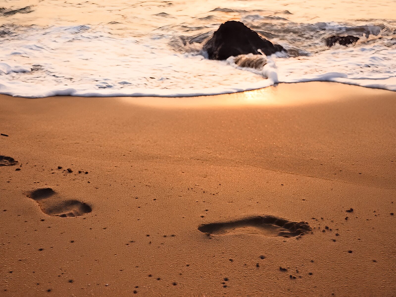 Footprints in the wet sand of Cola Beach as a wave draws back